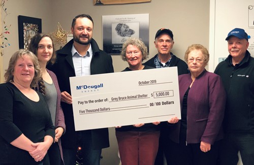 Shows 7 people inside house holding a large cheque from McDougall Energy