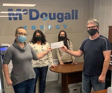 Shows a group of 4 people standing and holding a cheque wearing face masks against wall with McDougall Energy logo