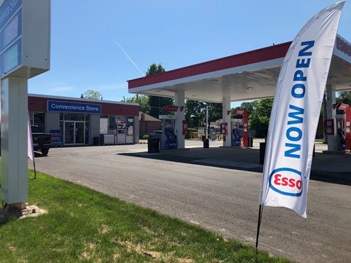Shows exterior shot of Esso gas station with a large stake banner with words Esso Now Open