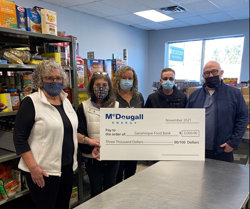 Shot of 5 people standing indoors at a food bank wearing face masks holding a large cheque from McDougall Energy