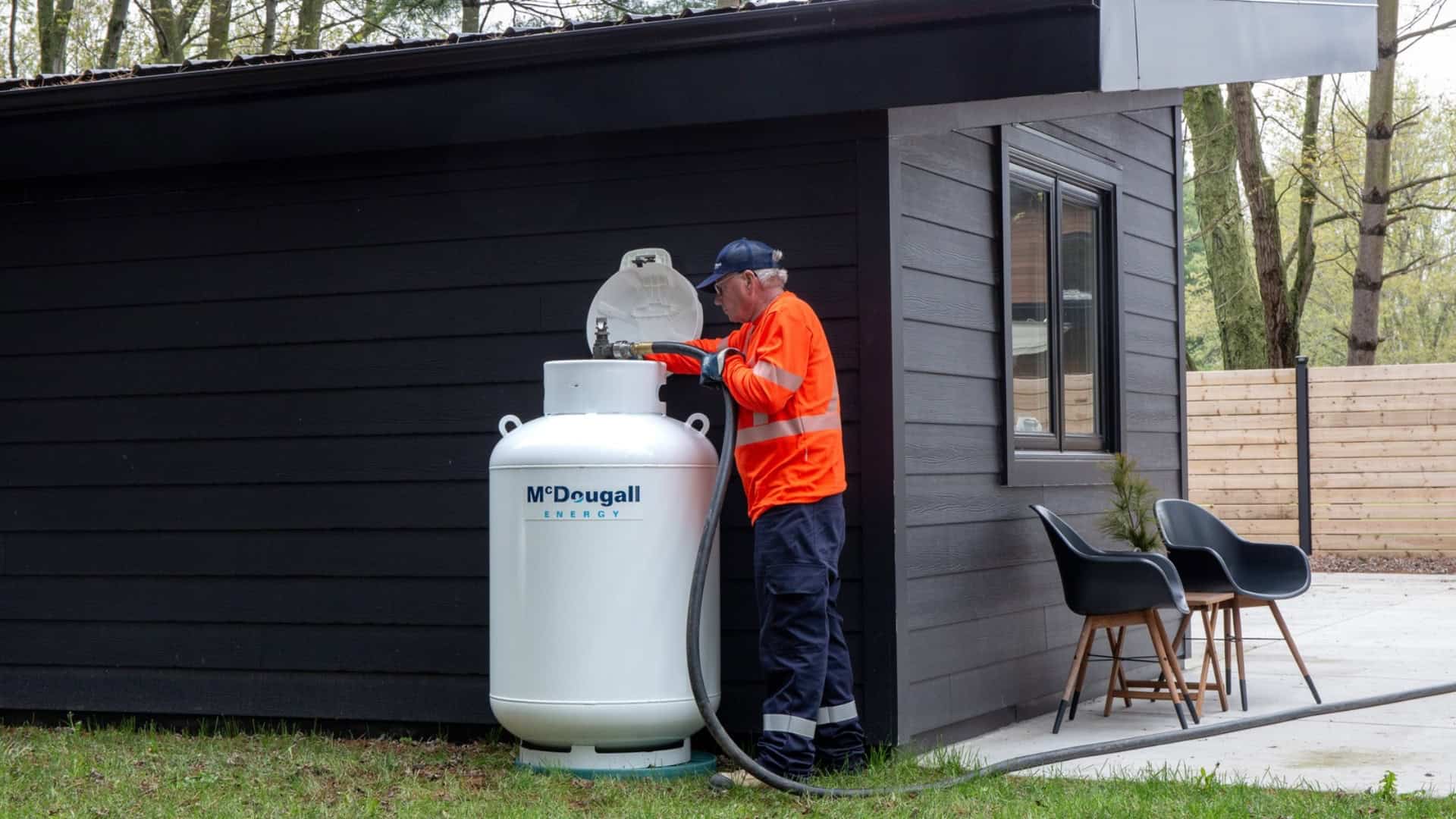 Technician refilling a propane tank outside a black building.
