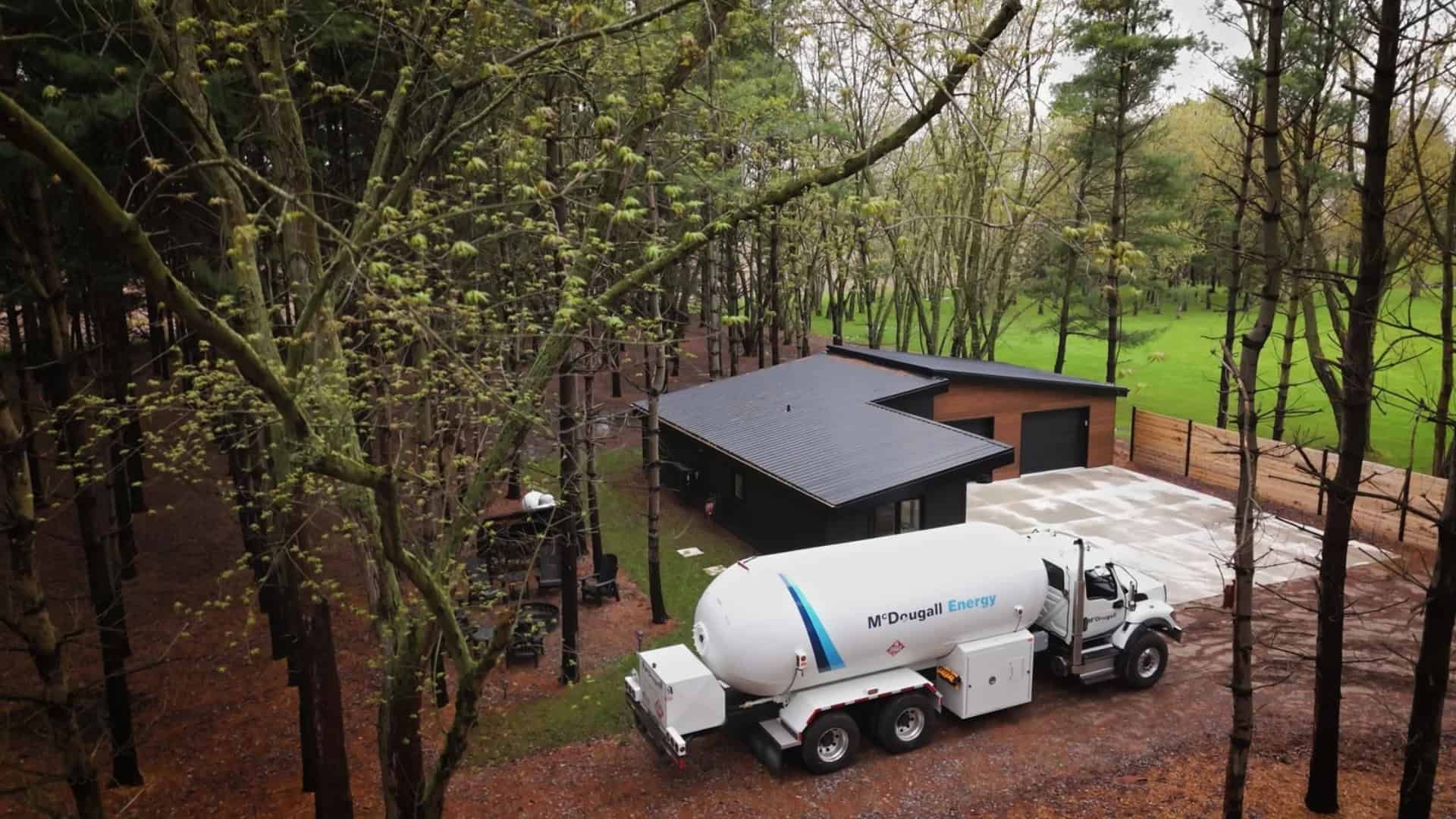 McDougall Energy propane delivery truck at modern residence in Ontario surrounded by trees in a wooded area.