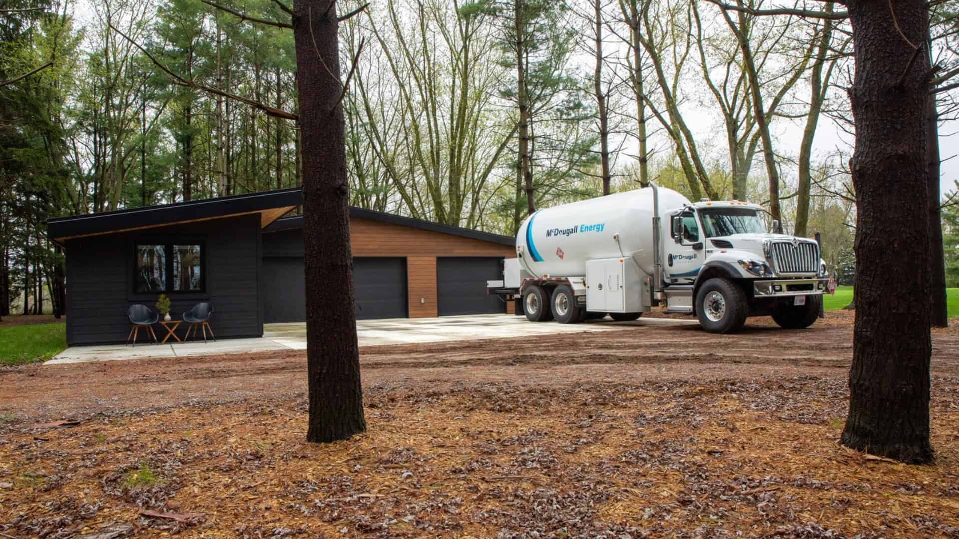 Fuel delivery truck at a modern home in a wooded area.