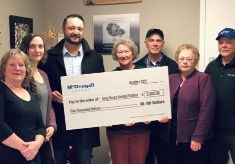 Shows 7 people inside house holding a large cheque from McDougall Energy