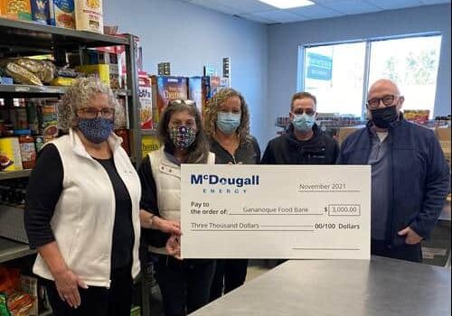 Shot of 5 people standing indoors at a food bank wearing face masks holding a large cheque from McDougall Energy