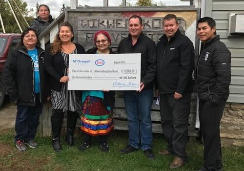 Shows 7 people outside holding a large cheque from McDougall Energy
