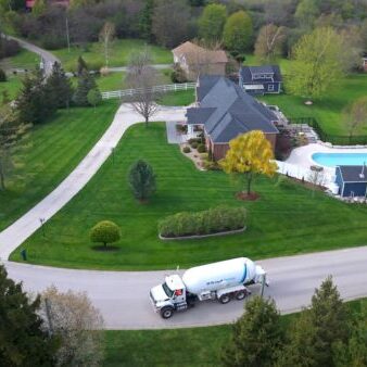 Fuel delivery truck on residential driveway, home with pool, lush landscaping, McDougall Energy fuel services, eco-friendly home.