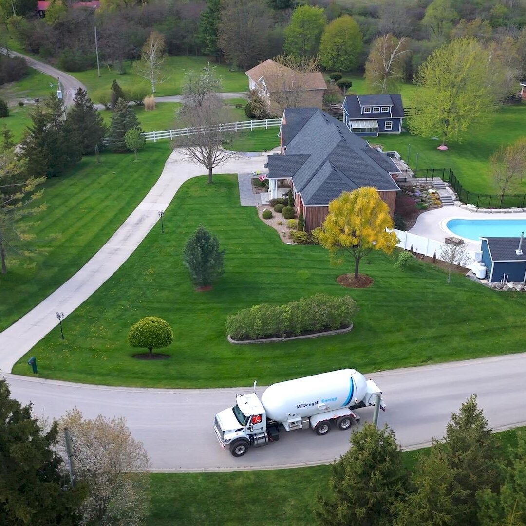 Fuel delivery truck on residential driveway, home with pool, lush landscaping, McDougall Energy fuel services, eco-friendly home.