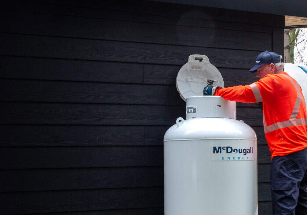 Technician refilling residential fuel tank outdoors.