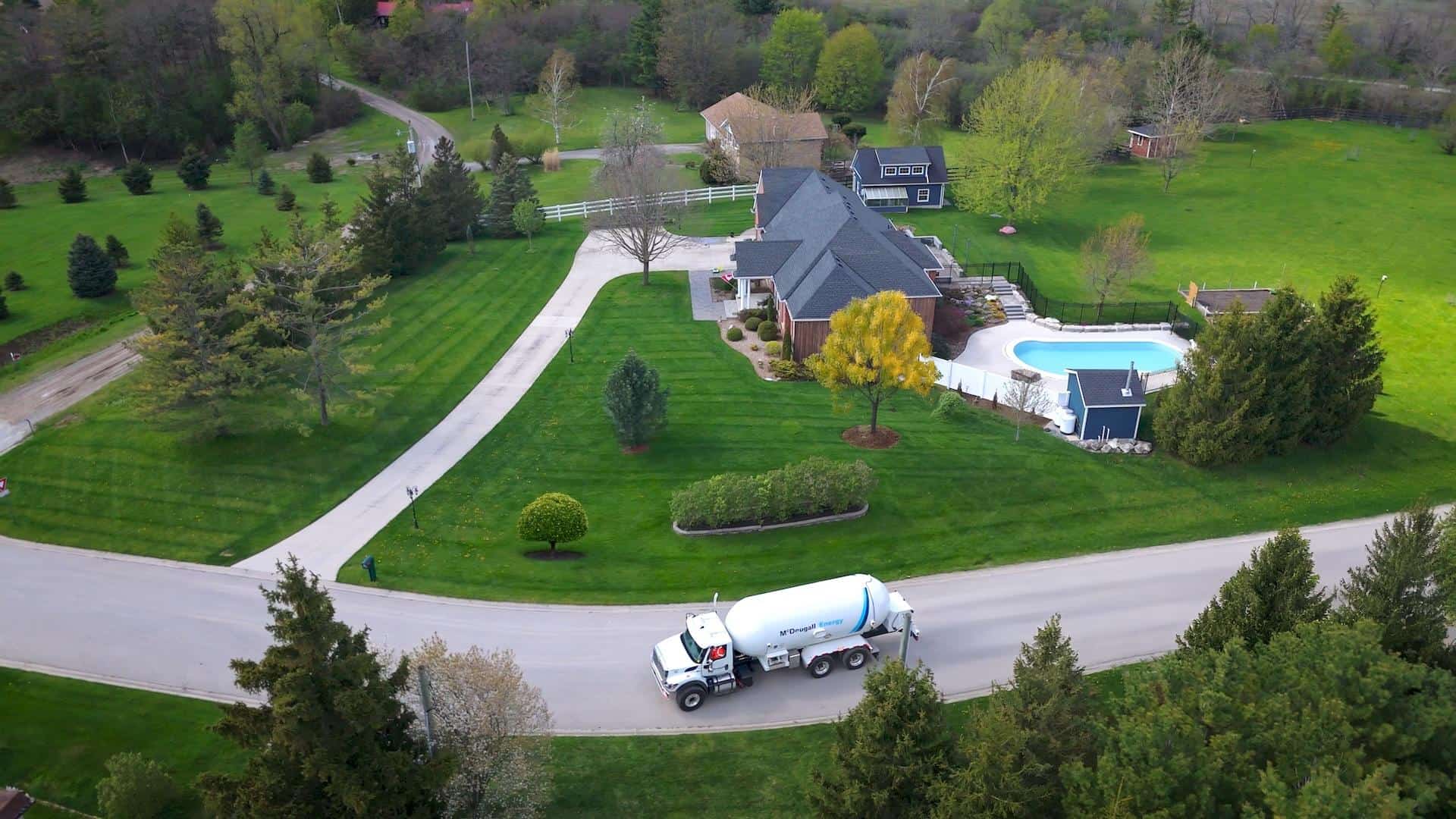 McDougall Energy propane delivery truck on residential driveway, home with pool, lush landscaping.